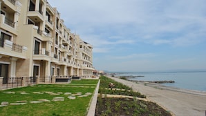 Une rangée d’immeubles à plusieurs étages dotés de balcons, une pelouse à l’avant et une plage en arrière-plan.