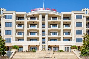 Un immeuble à plusieurs étages doté d’une entrée centrale, de balcons et d’une enseigne indiquant « GARDENIA PALACE ».