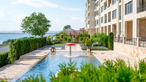 Une piscine ornée de deux statues de pingouins, entourée de verdure et bordée d’un bâtiment doté de balcons.