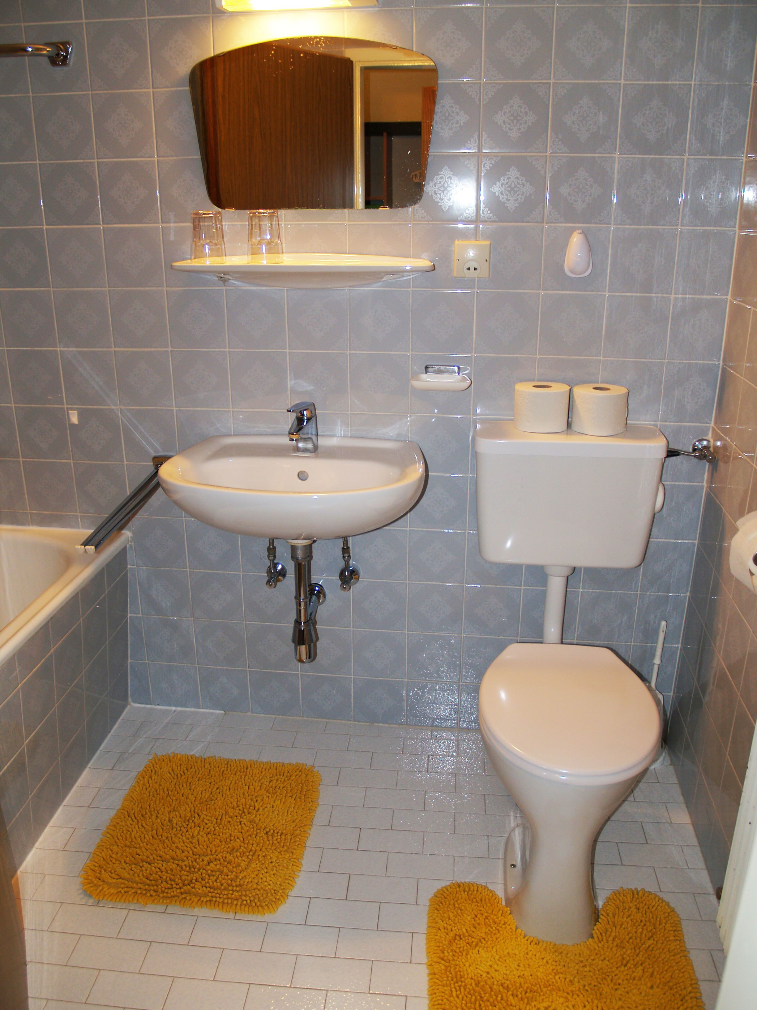 A bathroom with a sink, toilet, and bathtub. There are two yellow bath mats on the floor.