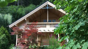 Een houten chalet met een balkon, omringd door weelderige begroeiing en bomen.