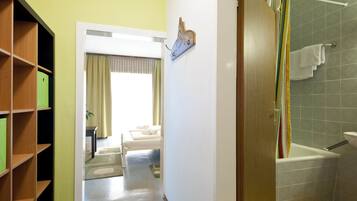 A hotel room with a wooden bookshelf, a bed with a beige headboard, a bathroom with a shower curtain, and a towel rack.