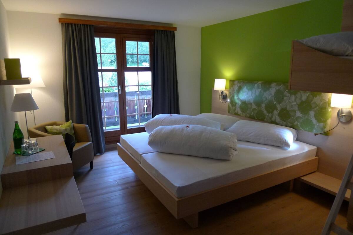 A hotel room with a bed, bedside tables, a desk, and a window with curtains.