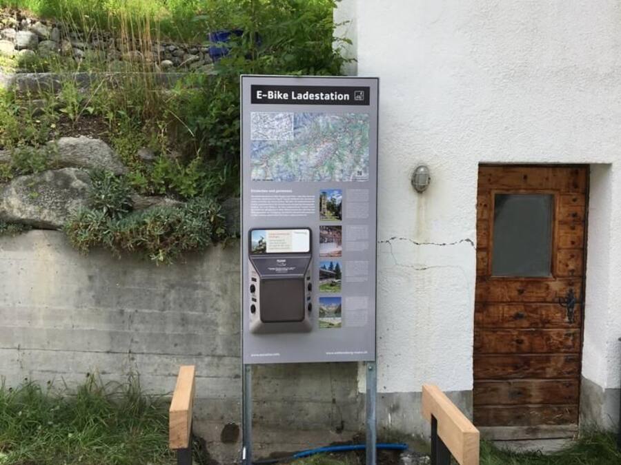 An E-Bike Station with a map and information panel, a wooden door, and a concrete wall.