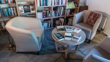 Un coin lecture accueillant avec deux fauteuils, une petite table ronde sur laquelle sont posés des livres et une bibliothèque remplie d’ouvrages.