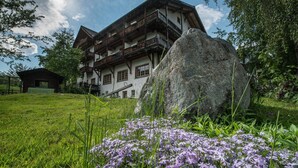 Eine traditionelle Chalet mit mehreren Balkonen, umgeben von üppigem Grün und violetten Blumen.