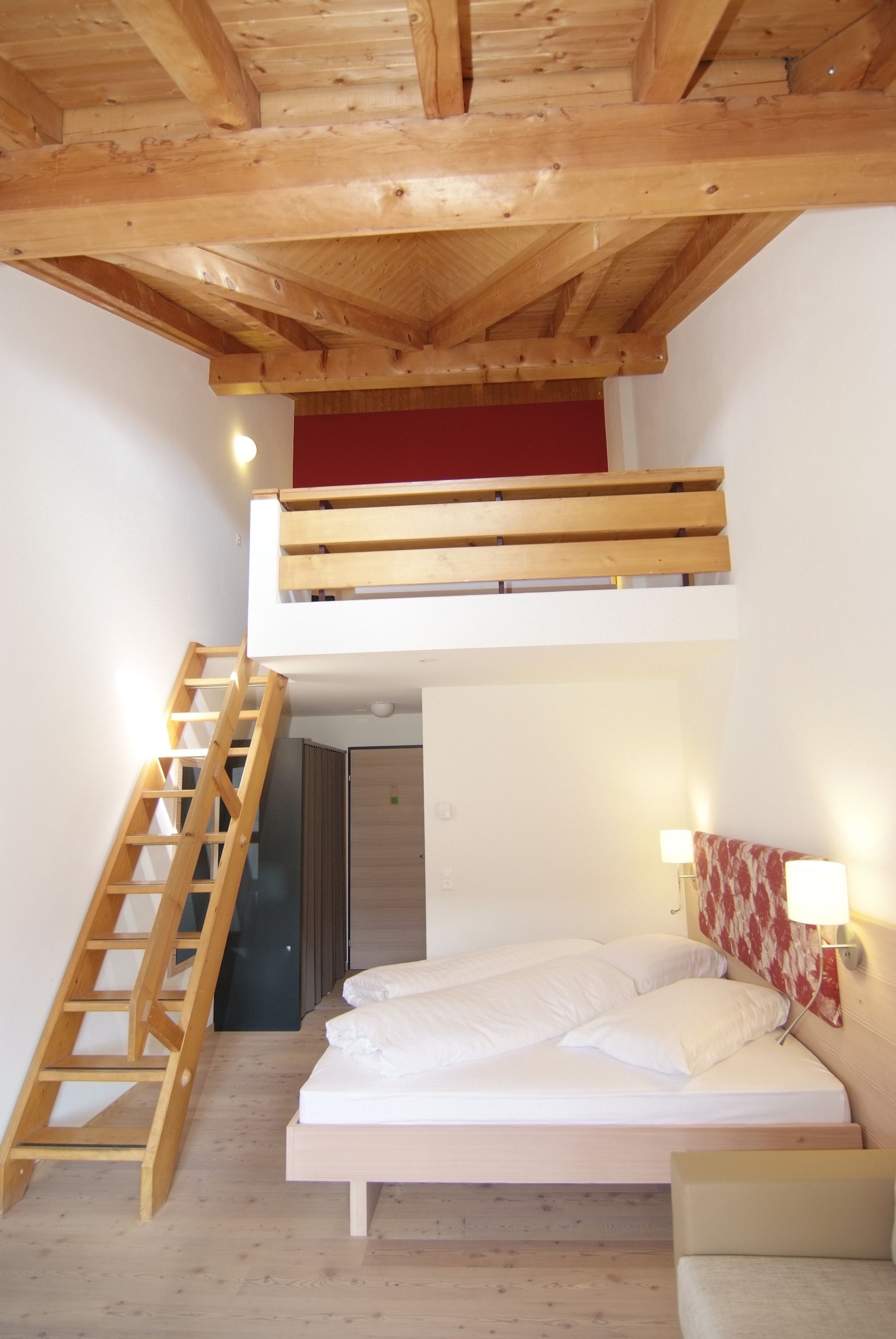 A loft bedroom with a wooden ladder leading to a bunk bed, a desk, and a chair.