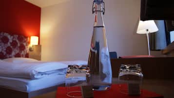 Ein Hotelzimmer mit Bett, Nachttisch mit Lampe und Tisch mit Flasche und Gläsern.
