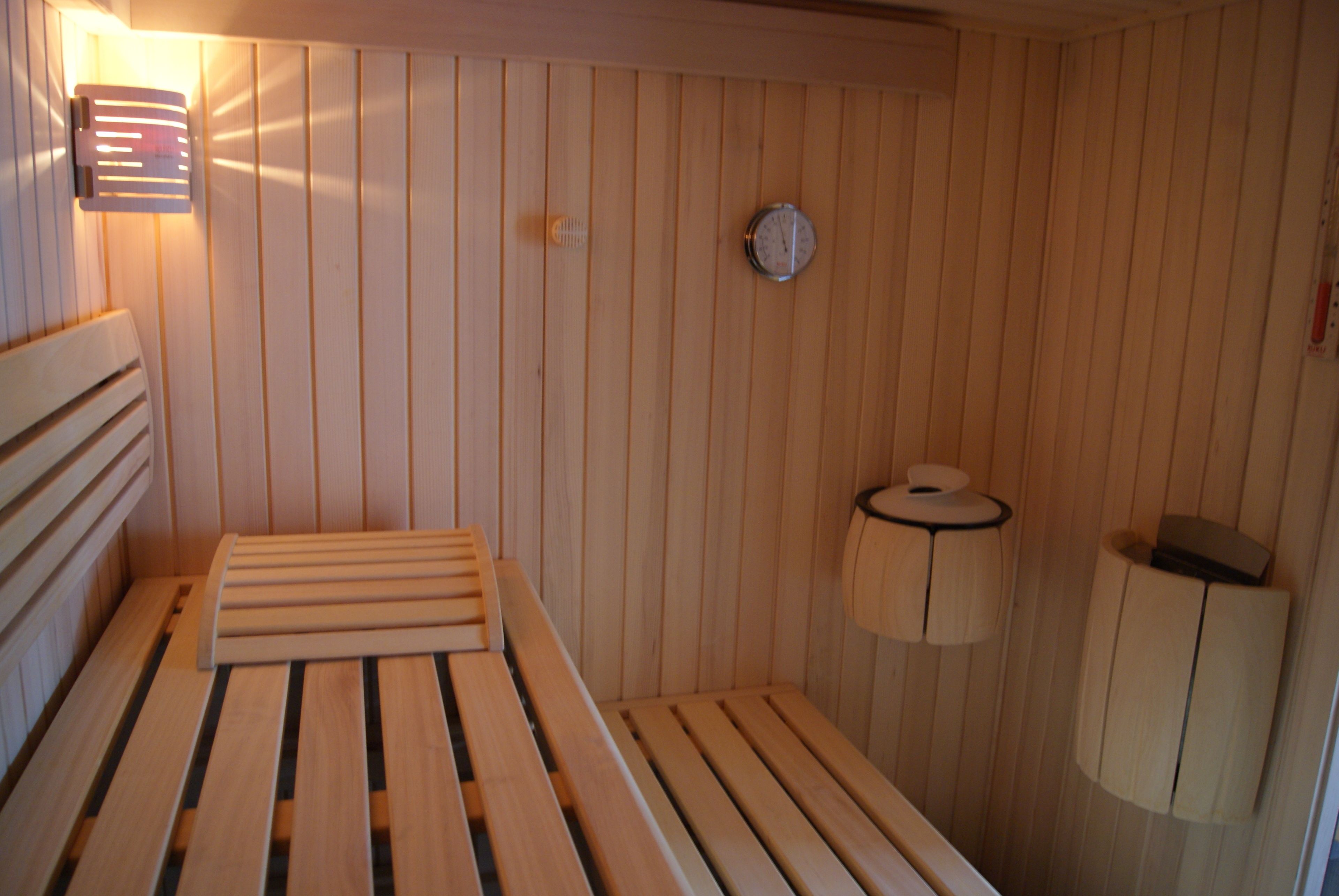 Una sauna de madera con bancos, un calentador en la pared, un reloj y un dispensador de toallas.
