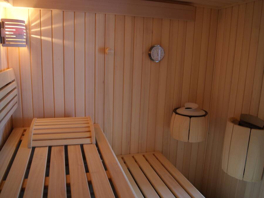 Una sauna de madera con bancos, un calentador en la pared, un reloj y un dispensador de toallas.