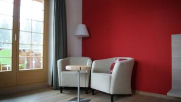 Une pièce avec un mur rouge, une porte à panneaux de verre, un fauteuil beige, une petite table ronde et un lampadaire.