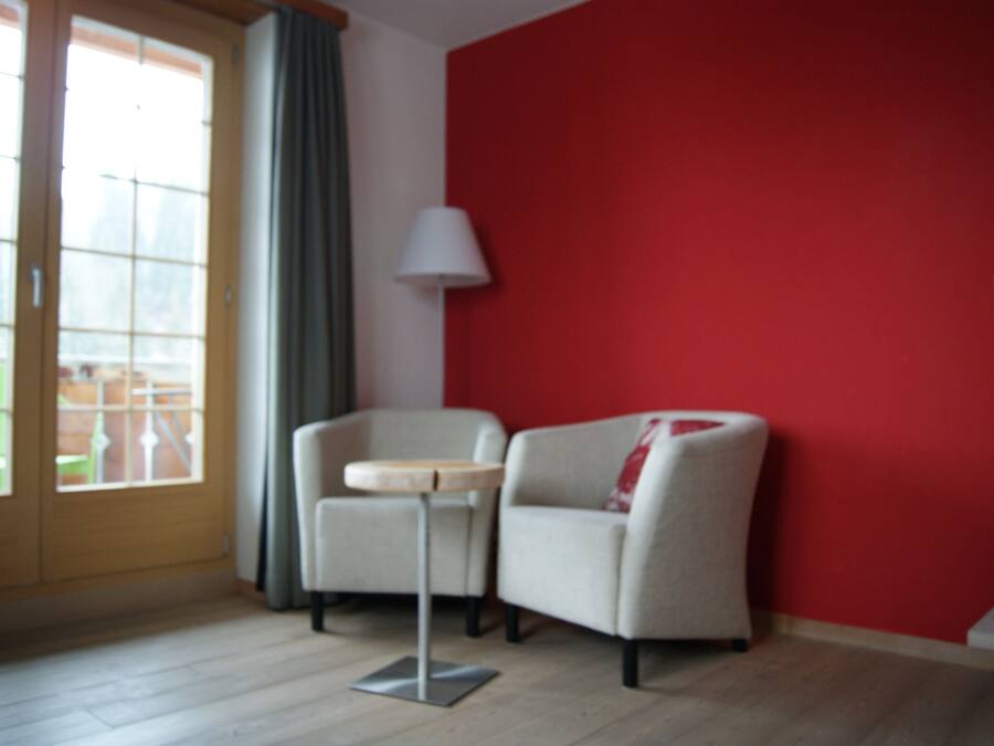 Une pièce avec un mur rouge, une porte à panneaux de verre, un fauteuil beige, une petite table ronde et un lampadaire.