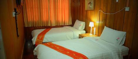 A hotel room with two beds, wooden walls, a window with curtains, a bedside lamp, and a wall-mounted phone.