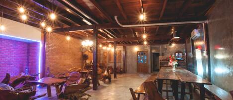 A rustic interior with exposed wooden beams, a long wooden bar, and unique wooden chairs.
