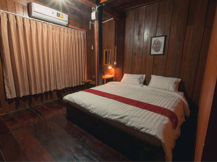 A wooden-paneled room with a bed, an air conditioning unit, a lamp, and a framed picture on the wall.