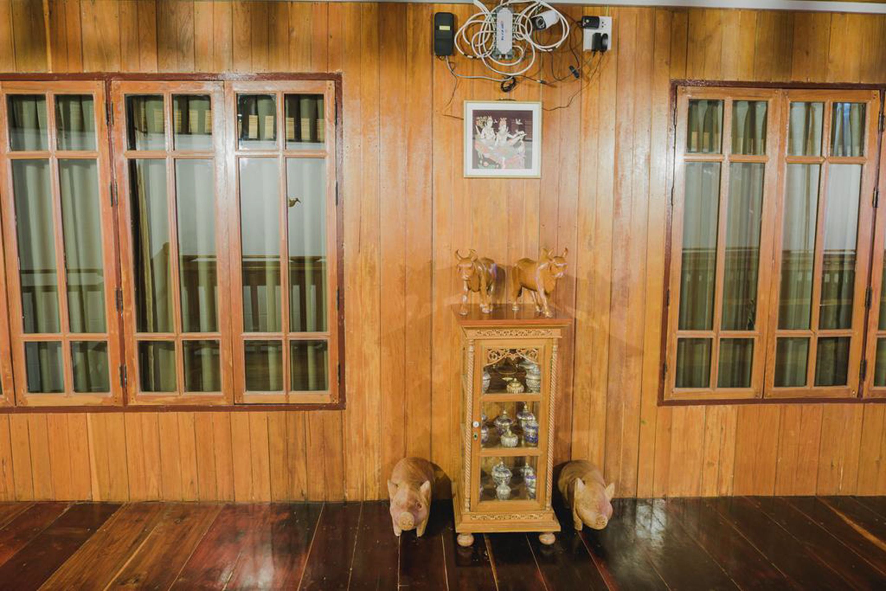 A room with wooden paneled walls, a wooden cabinet with glass doors, and two pig statues.
