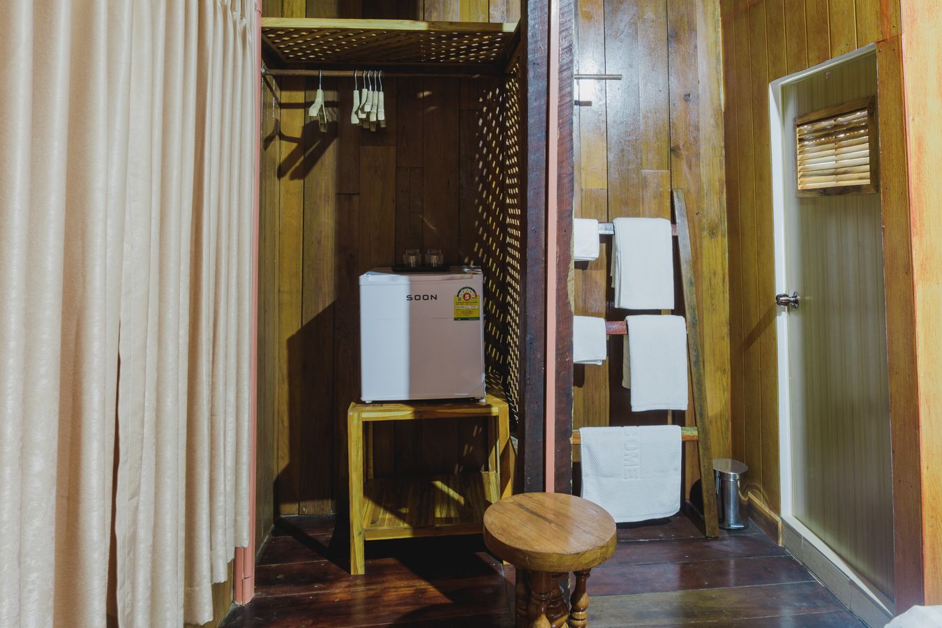 A wooden interior with a white refrigerator, a wooden stool, and a metal trash can.