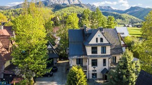 A traditional chalet with a sloped roof, surrounded by lush greenery and a mountain backdrop. - Szarotka (Zakopane)