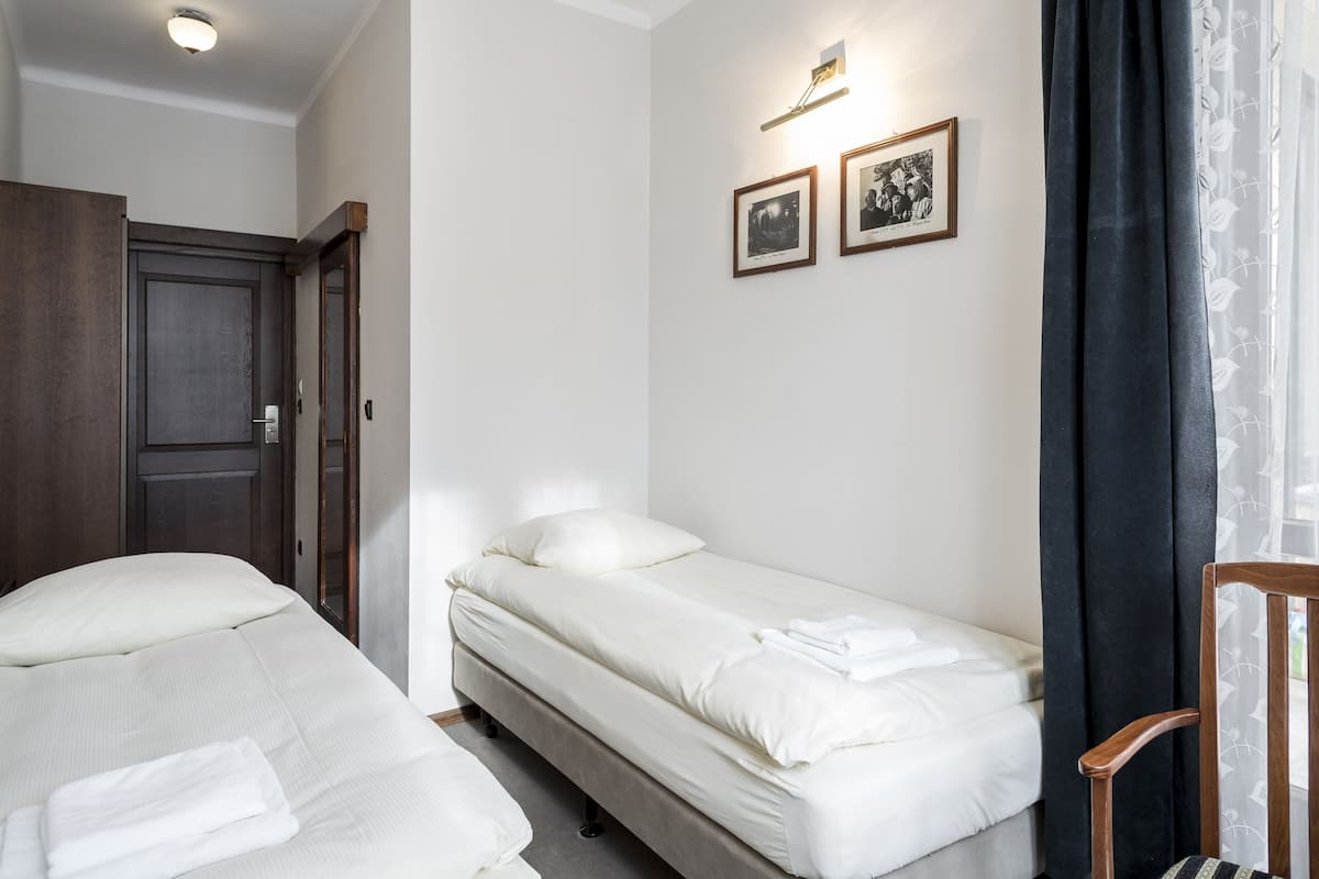 Habitación de hotel con dos camas, un armario de madera, una mesita pequeña y dos cuadros en la pared.