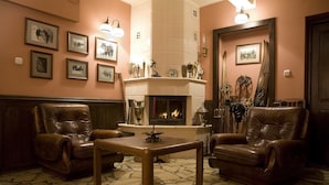 A cozy room with a fireplace, leather armchairs, a wooden table, and framed pictures on the walls. - Szarotka (Zakopane)