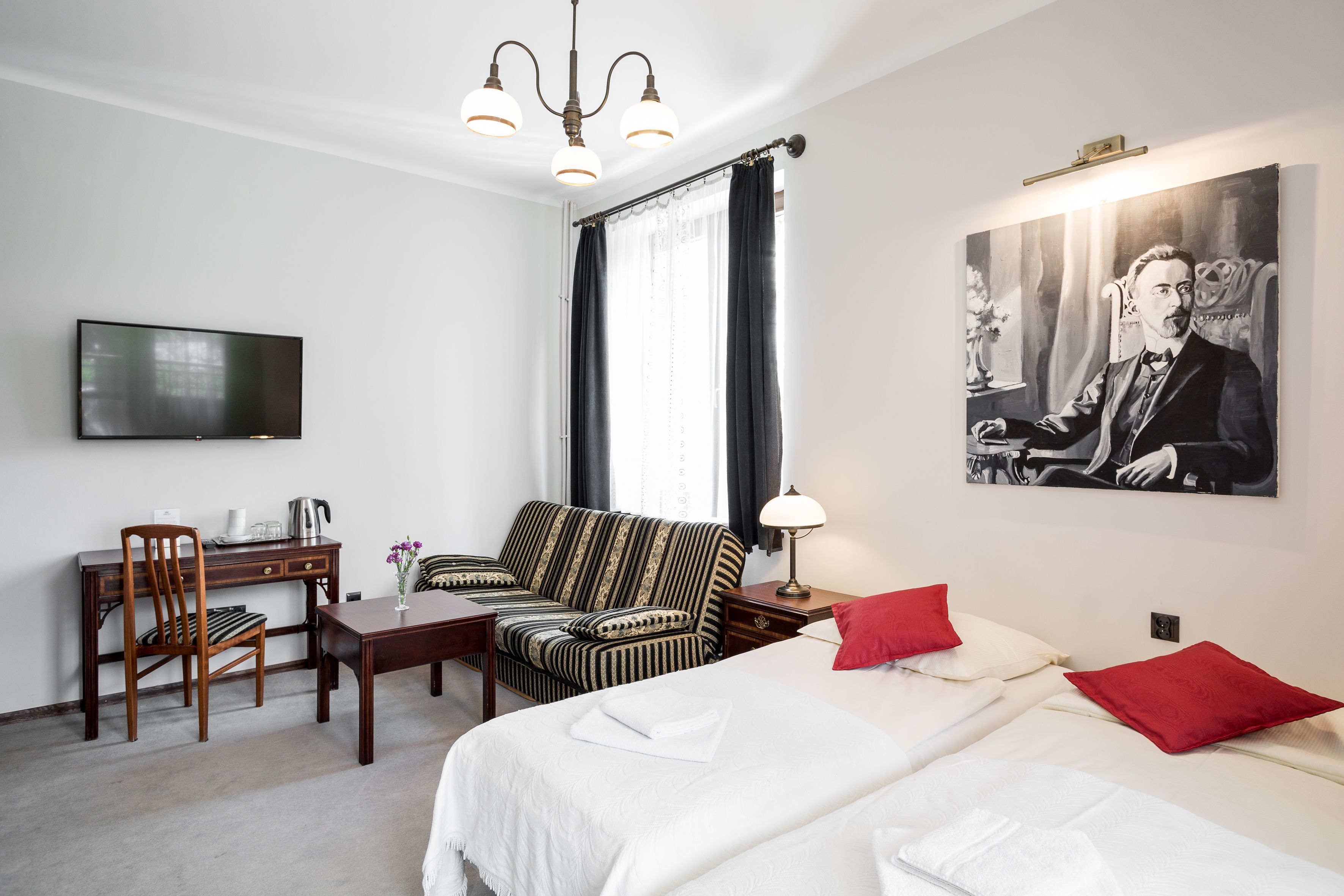 Habitación de hotel con cama, sofá, escritorio con silla, televisor y un cuadro en la pared.
