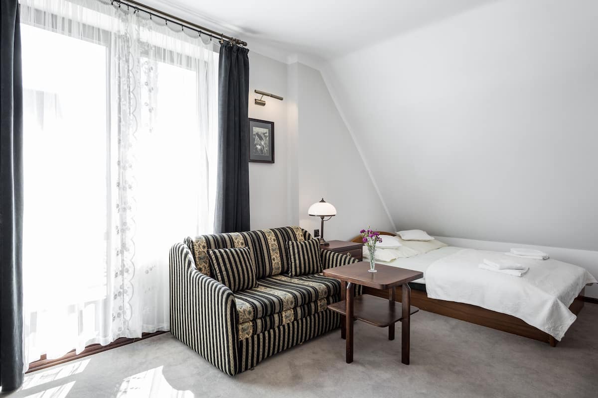 Una habitación de hotel con sofá, una mesita, una cama y un ventanal con cortinas.