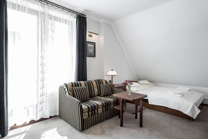 Una habitación de hotel con sofá, una mesita, una cama y un ventanal con cortinas.