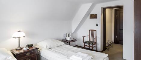 A hotel room with a bed, a bedside table with a lamp, a chair, and a small table with a coffee maker and glasses.