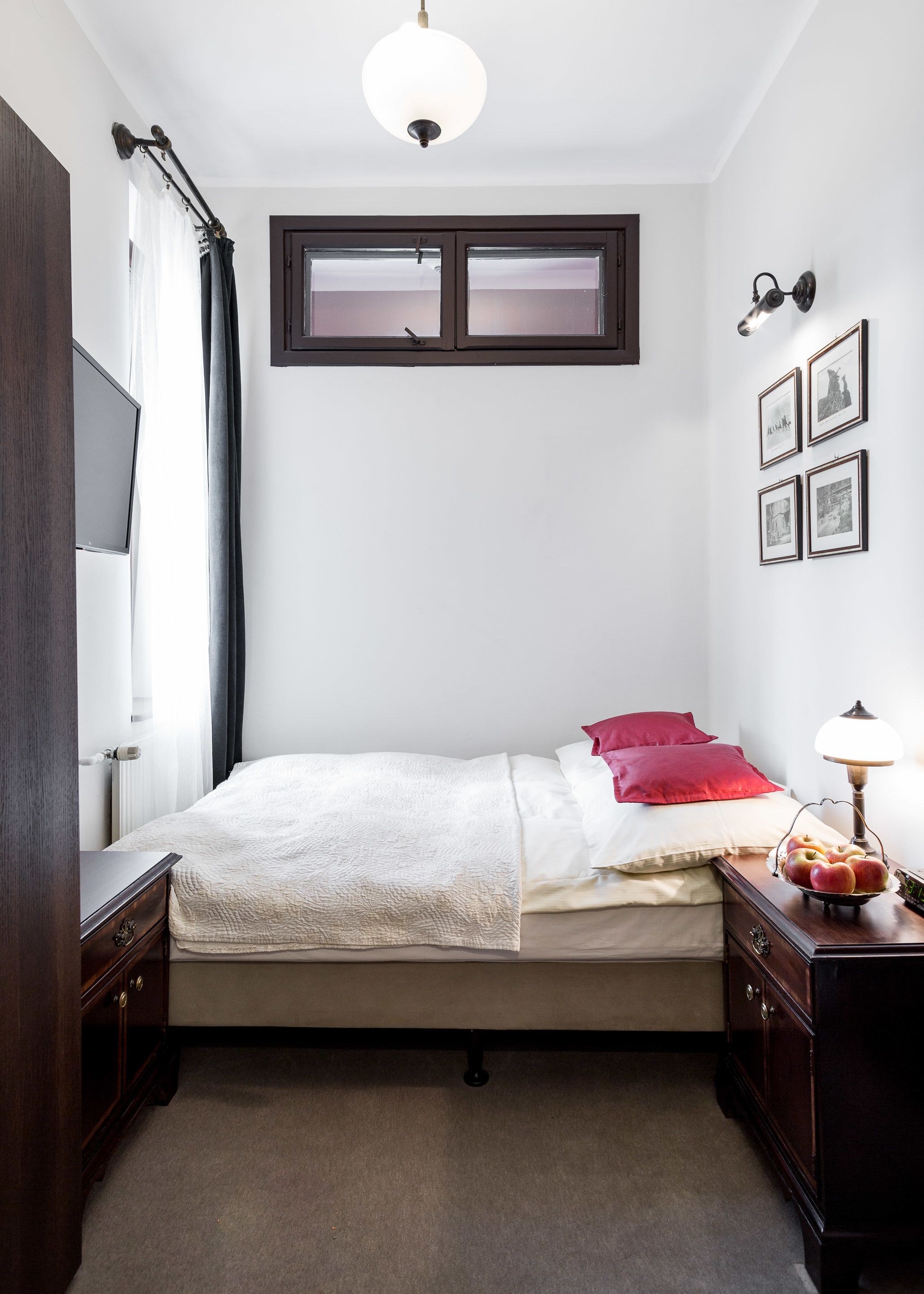 A bedroom with a bed, a nightstand, a lamp, a window, and a wall-mounted picture frame.