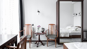 A hotel room with a wooden desk, two chairs, a round table with a tray of items, a bed with white bedding, a large mirror, and a wall-mounted light fixture. - Szarotka (Zakopane)