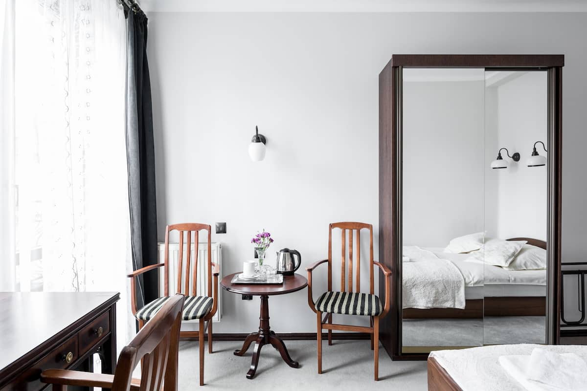 Una habitación de hotel con una cama, dos sillas, una mesita con una bandeja, una lámpara de pared y un espejo que refleja la cama.