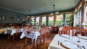 A restaurant with multiple tables set for dining, wooden chairs, and a view of greenery outside. - Szarotka (Zakopane)