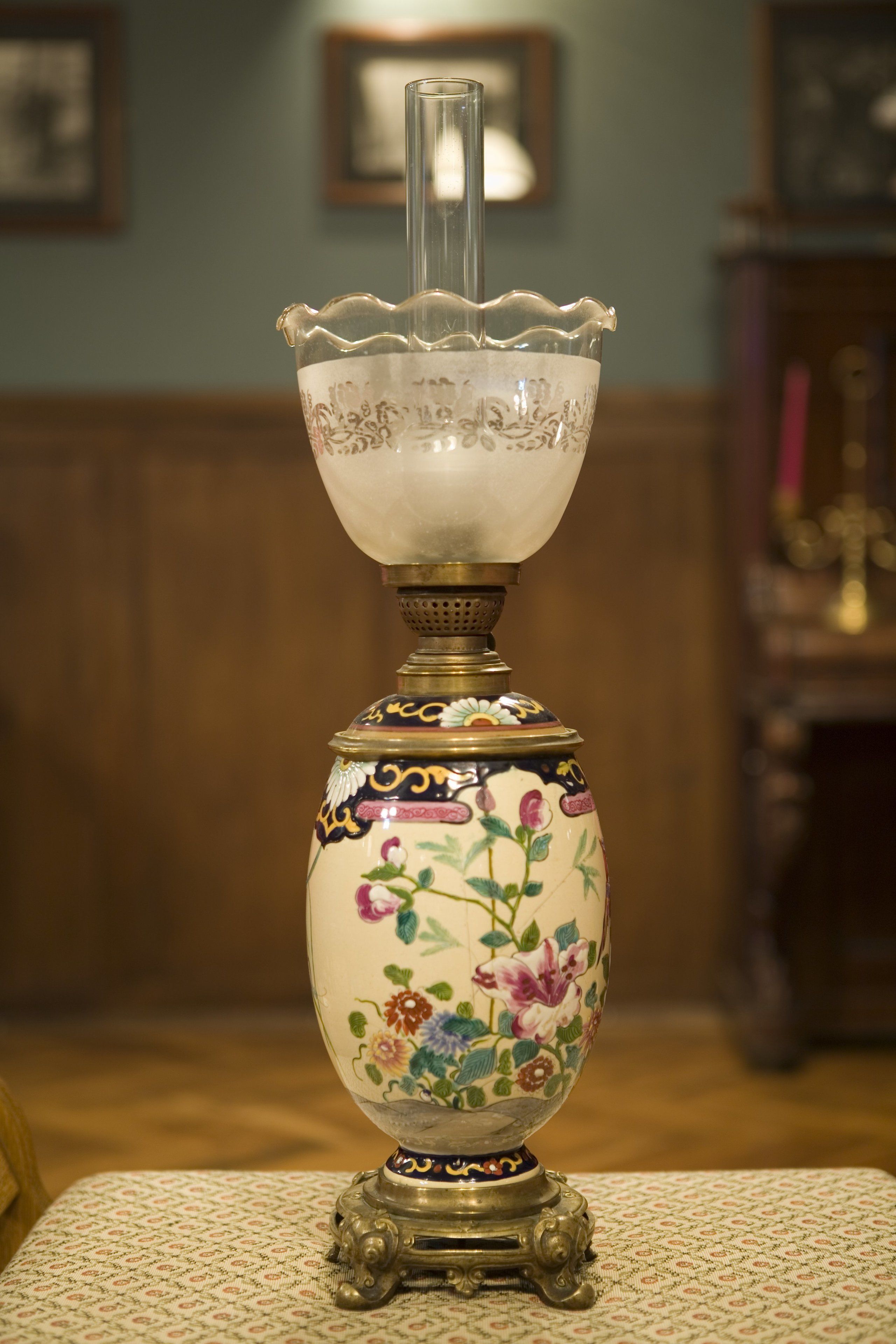 A table lamp with a floral design on the base, placed on a patterned tablecloth.