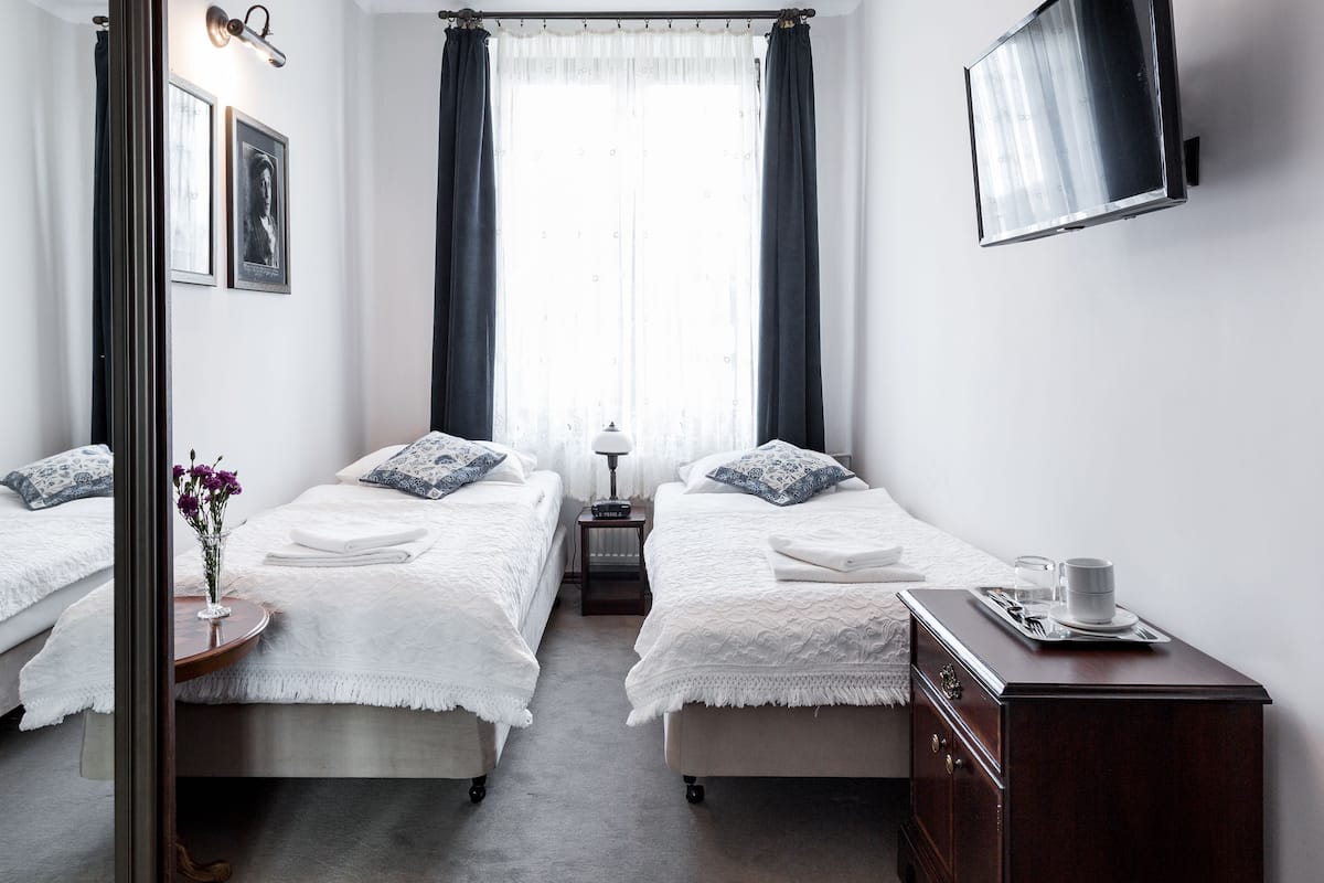 Una habitación de hotel con dos camas, un televisor, una mesita de noche y un espejo.