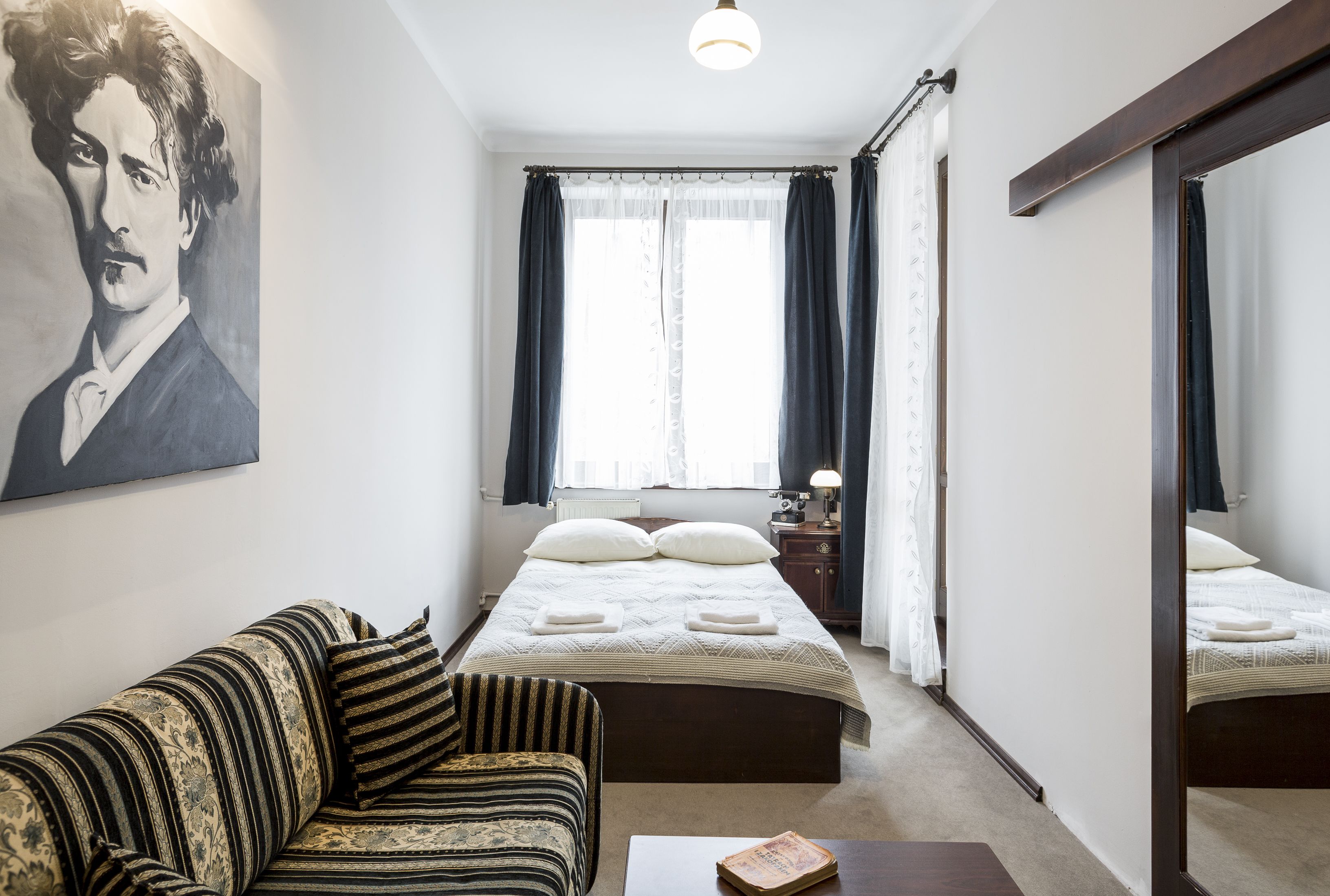 Een hotelkamer met een bed, een slaapbank, een nachtkastje, een lamp, een spiegel en een schilderij aan de muur.
