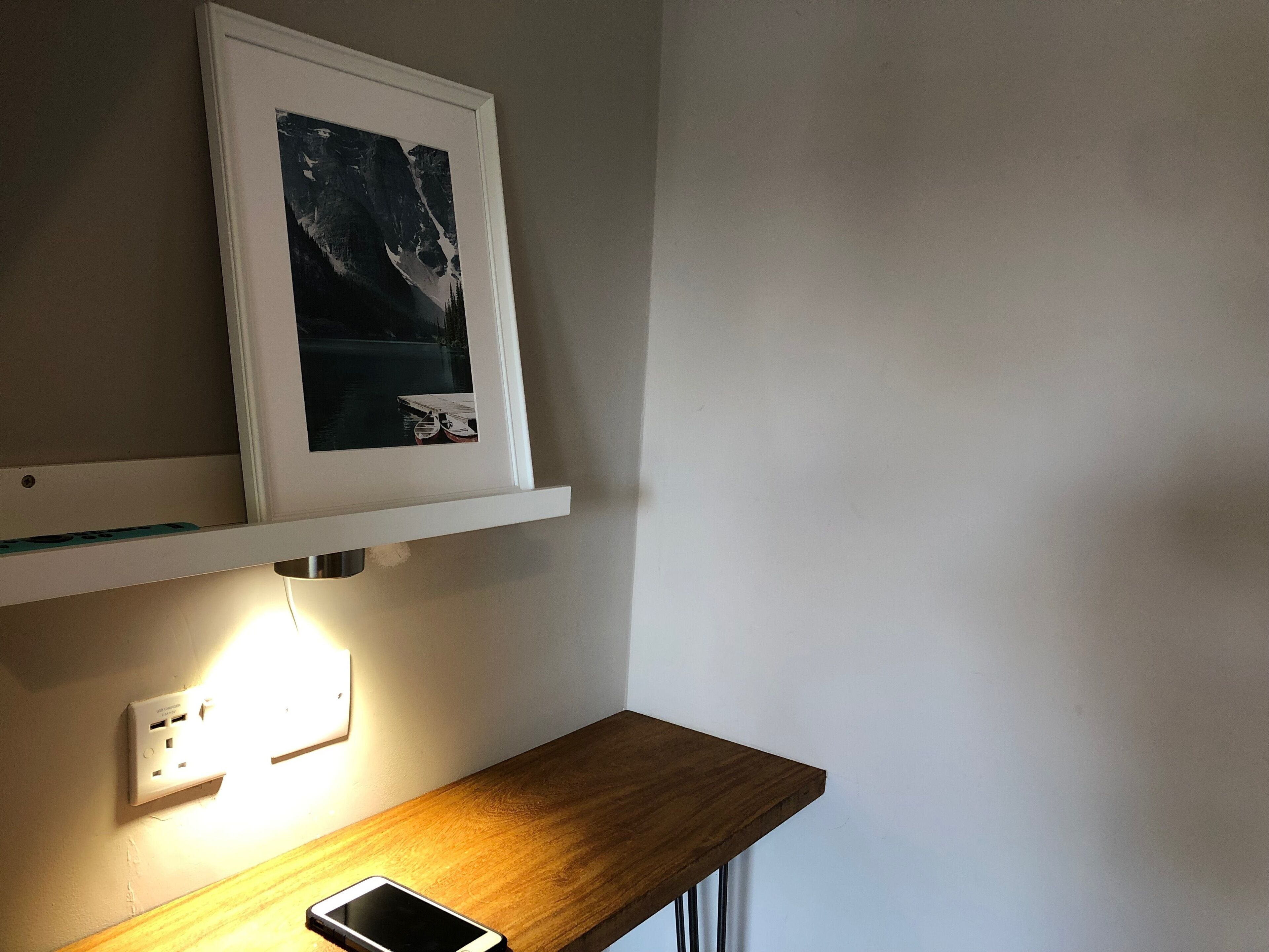 Une pièce avec un bureau en bois, un tableau encadré accroché au mur et une prise électrique.