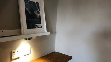 Une pièce avec un bureau en bois, un tableau encadré accroché au mur et une prise électrique.