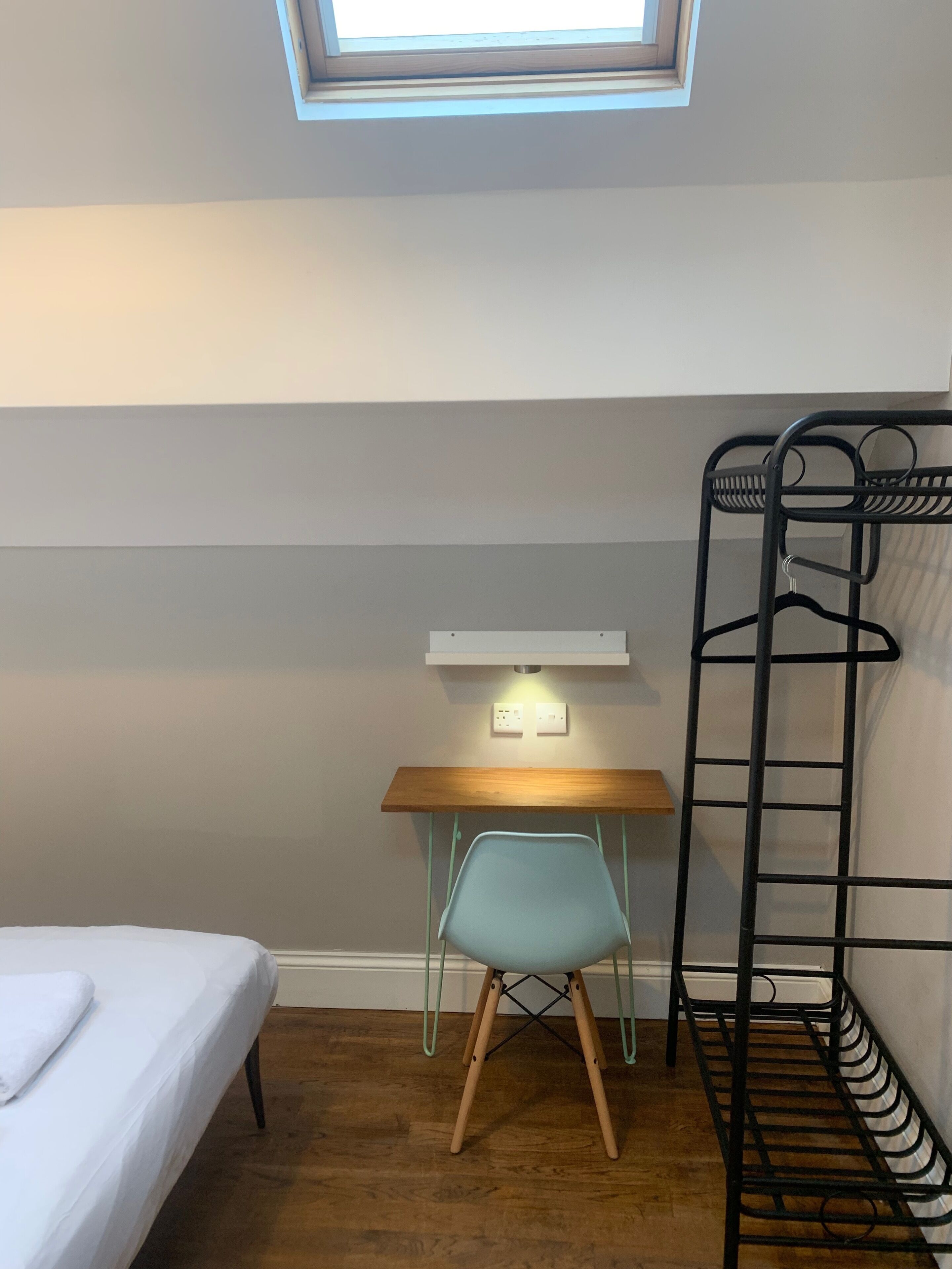 A dormitory room with a bunk bed, a desk with a chair, and a skylight above.