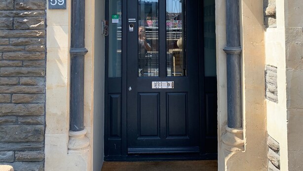 A black door with a gothic archway, a number '59' sign, and a stone wall. - The Riverhouse (Cardiff)