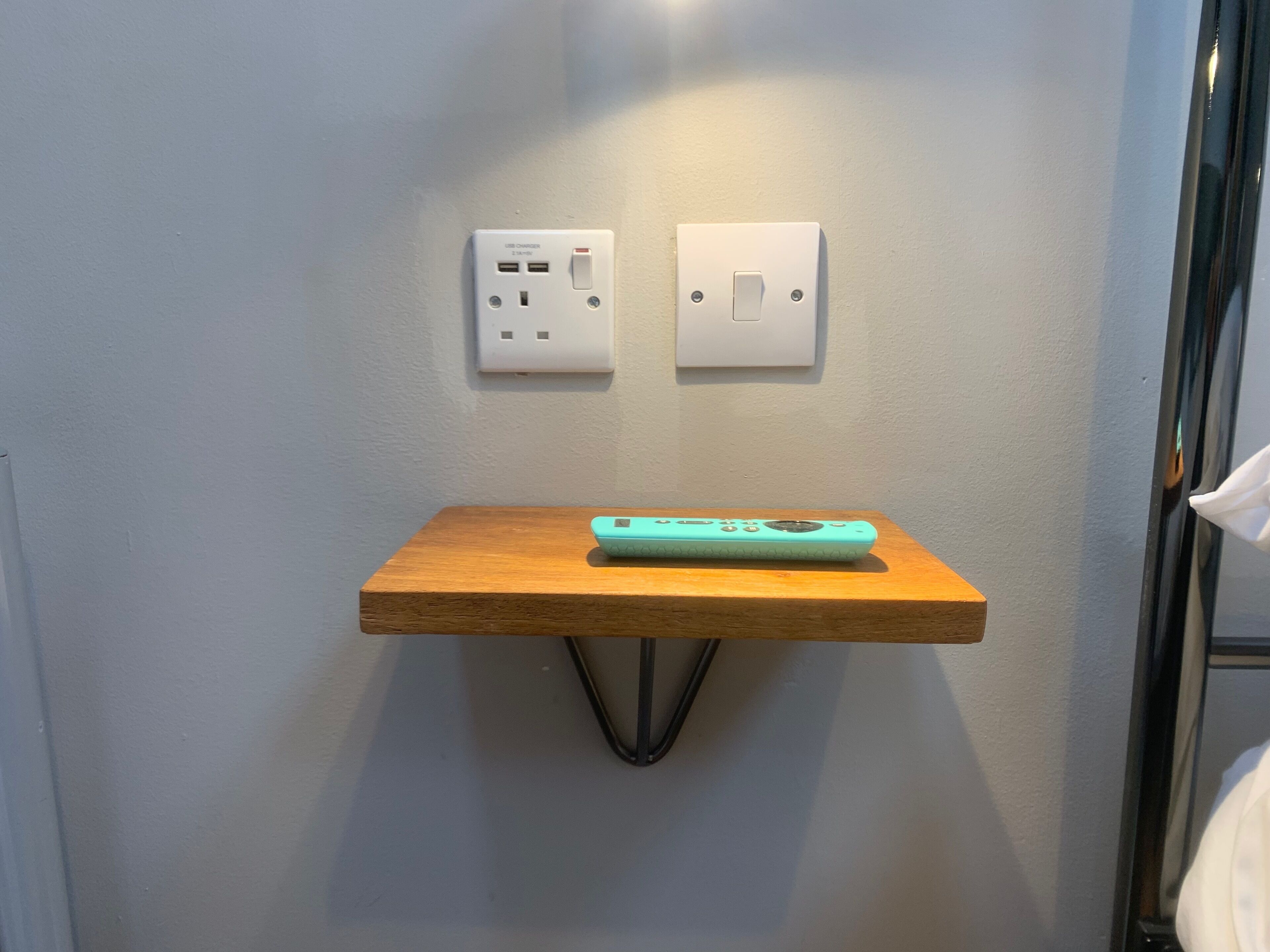 A small wooden table with a teal remote control on it, positioned between two wall-mounted electrical outlets.