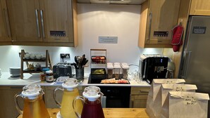 A kitchen with wooden cabinets, a coffee machine, a toaster, and a refrigerator. There are also three pitchers of beverages on the counter. - The Riverhouse (Cardiff)