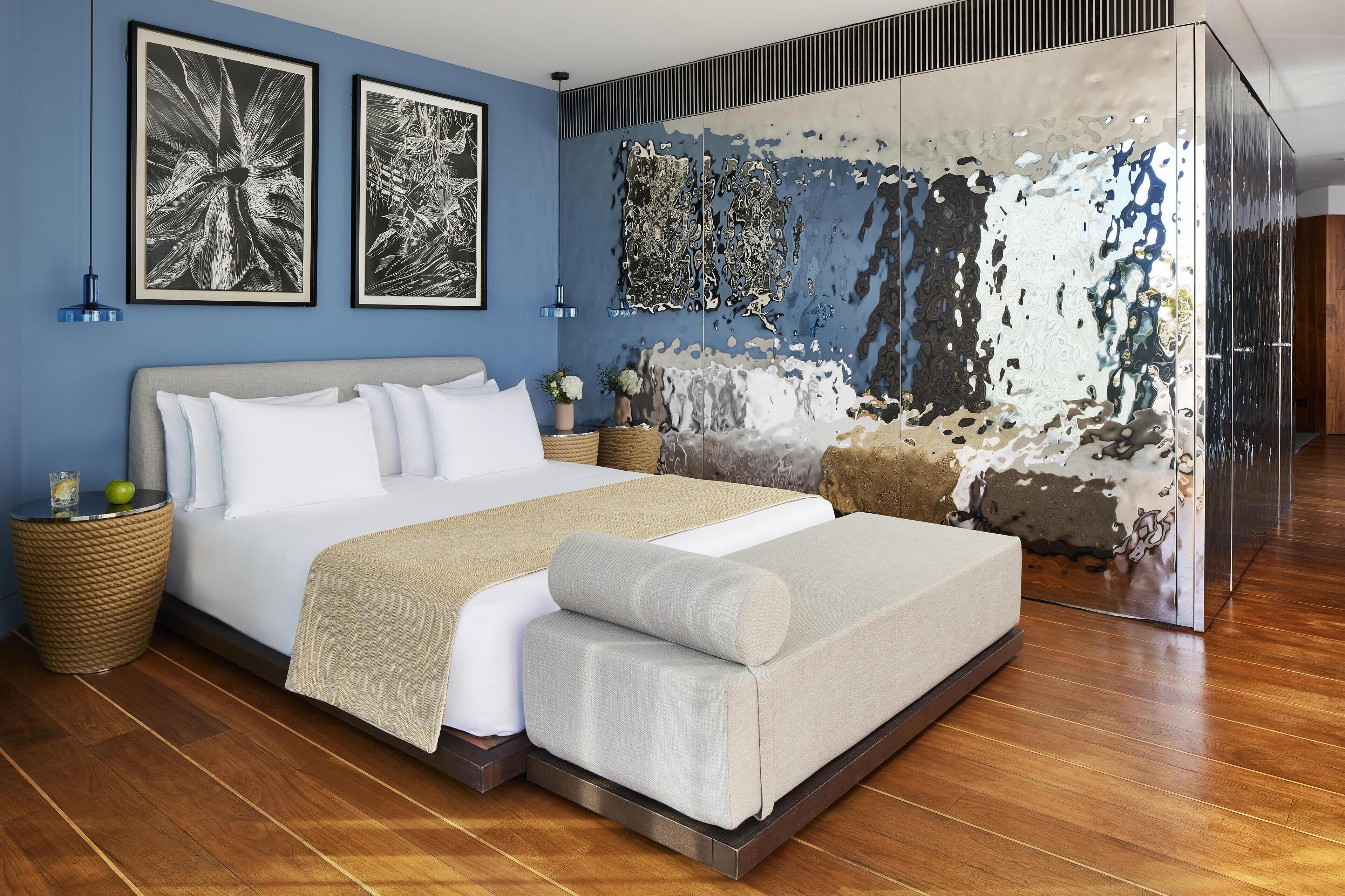 A modern bedroom with a large bed, a decorative mirror, and two framed artworks on the wall.