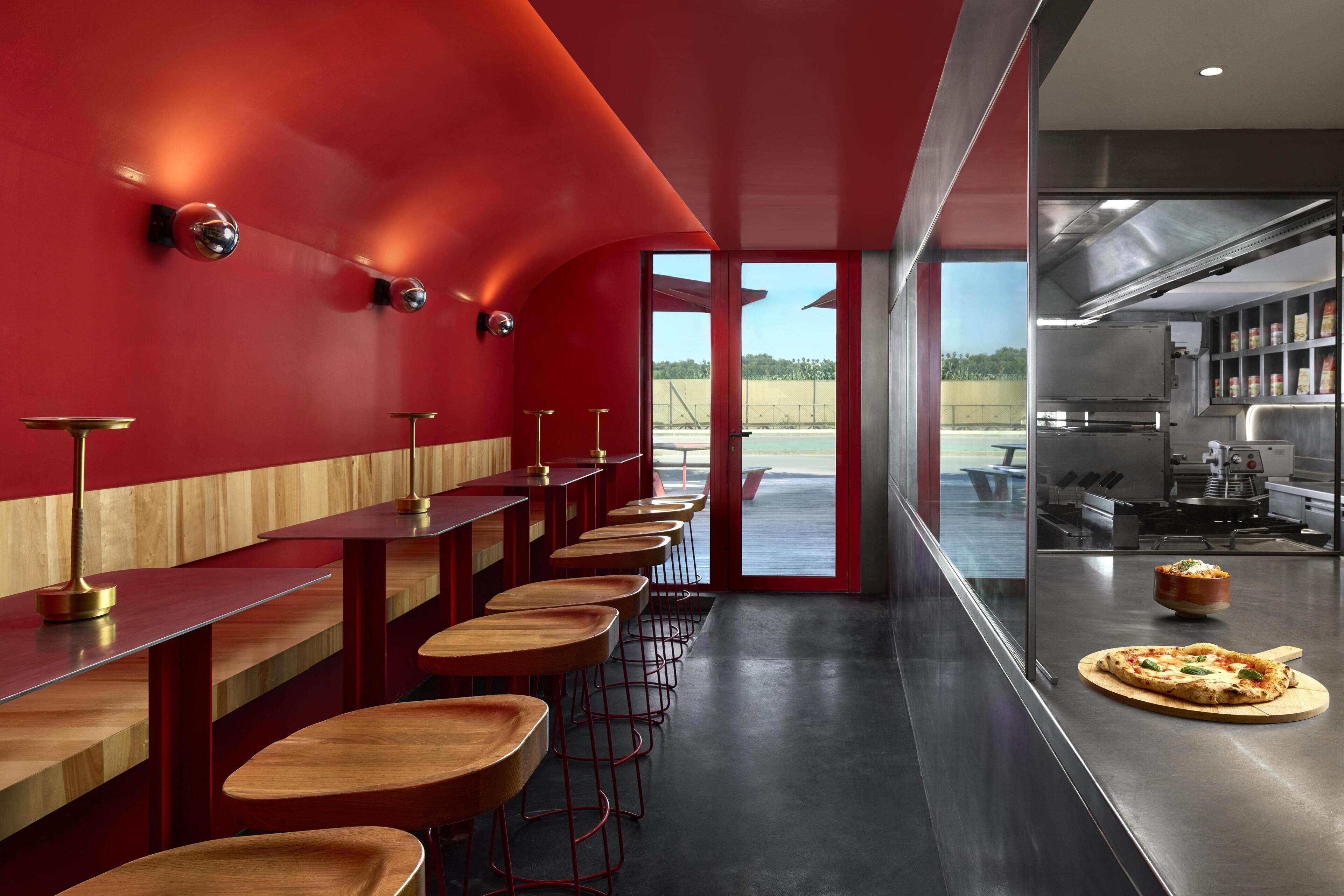 A modern bar area with red walls and wooden bar stools.