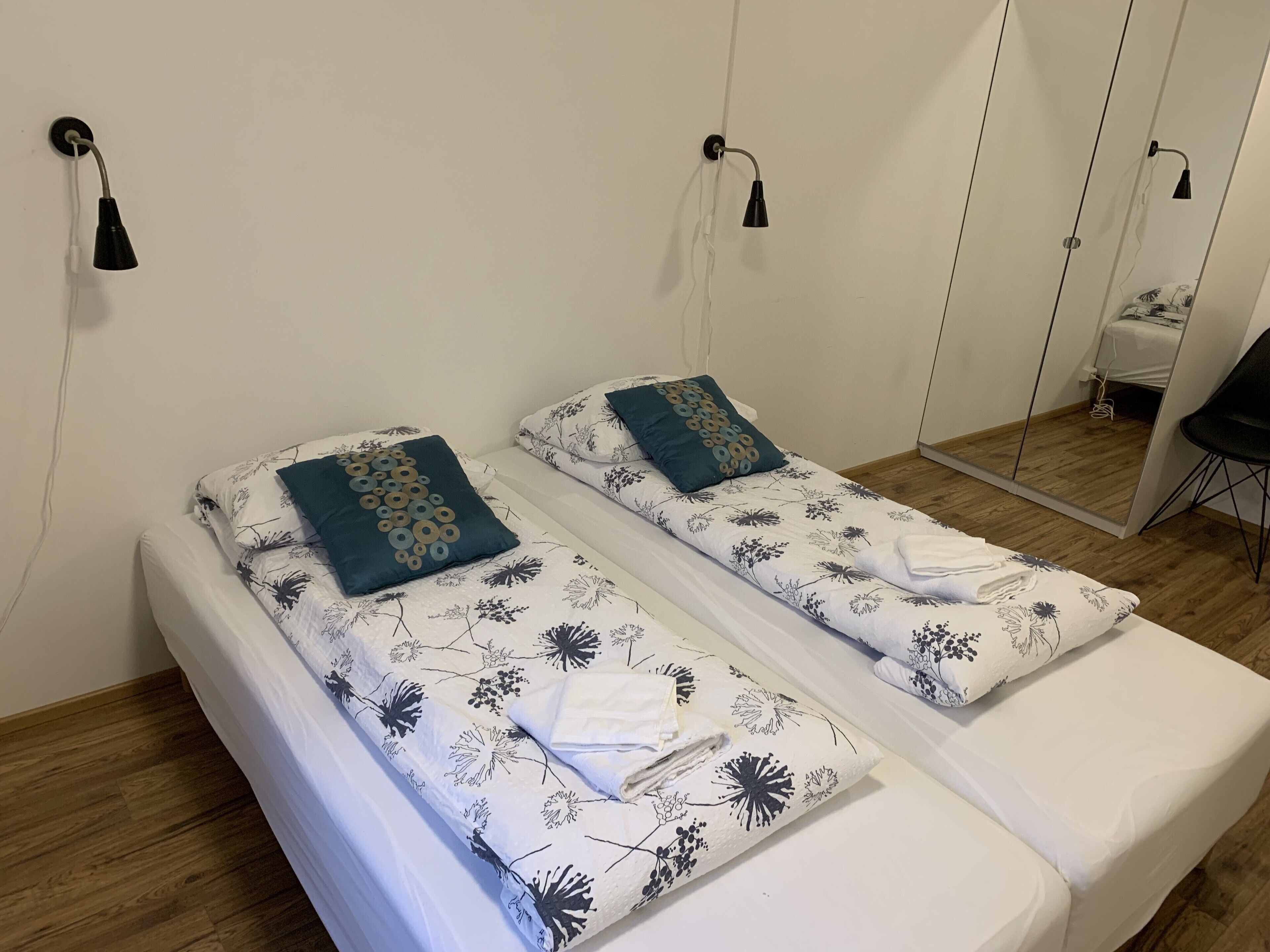 A double bed with floral bedding and two pillows, a bedside table, a mirror, and a black chair.