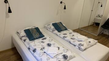 A double bed with floral bedding and two pillows, a bedside table, a mirror, and a black chair.