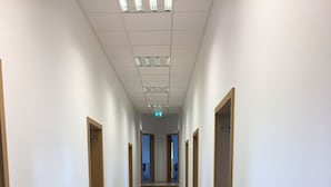 Un long couloir étroit, doté d’un plancher en bois et de murs blancs, qui mène à un escalier.