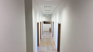 Un long couloir étroit, doté d’un plancher en bois et de murs blancs. Des portes se trouvent de part et d’autre du couloir, et un extincteur est fixé au mur.