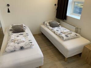 Two single beds with floral bedding, a wooden floor, a window with curtains, and a radiator.
