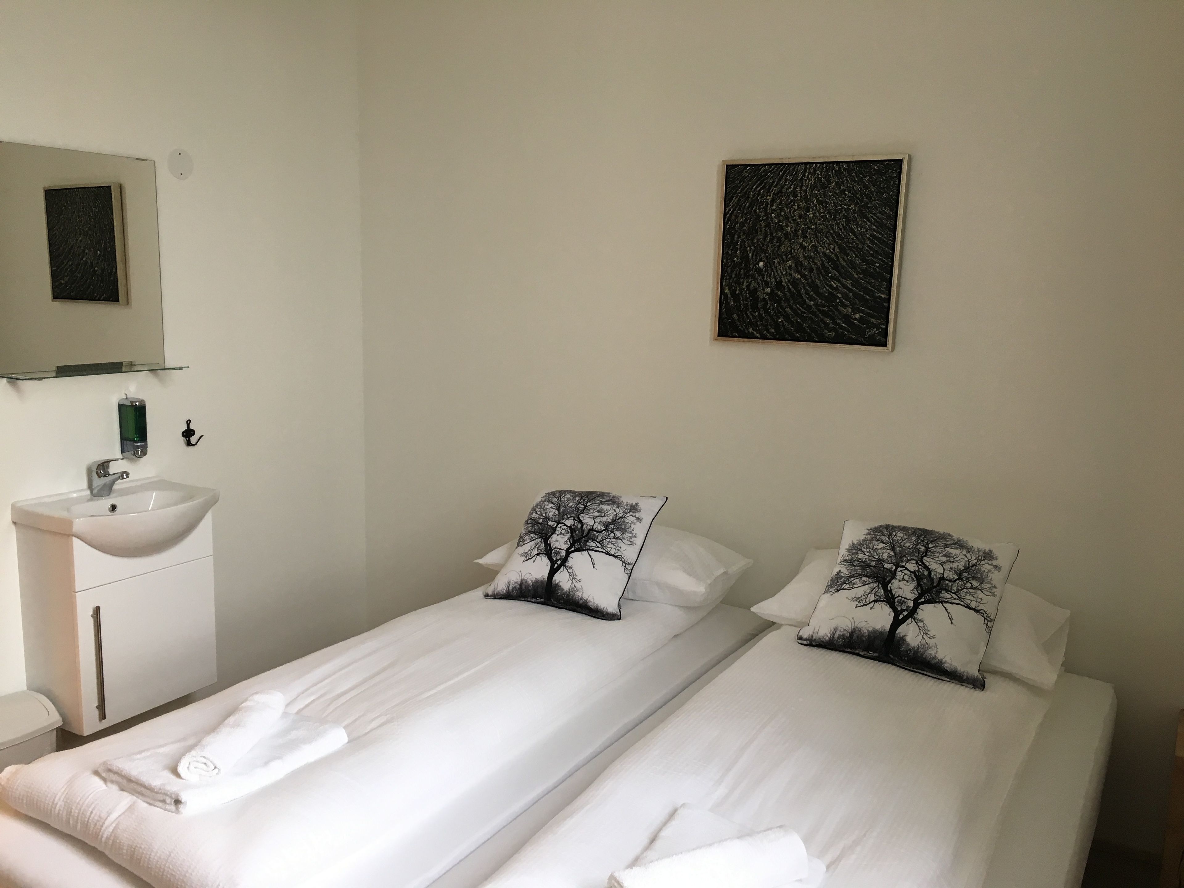A hotel room with two single beds, a white sink, and a mirror above it.