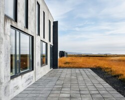 A modern building with large windows and a paved walkway leading to a grassy field.